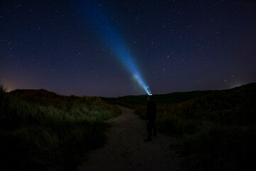 Adventurous man looking up at the stars on a beach path at night with his headlamp shinning up at the sky.