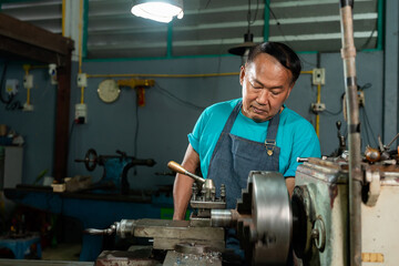 Portrait of a senior Asian man who is a blacksmith. Inspecting small steel turning tools. to prepare the lathe In the family's small lathe