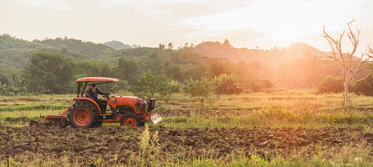 Tuinposter landbouwtractor met chauffeur die ploegt om de grond te vullen voor de teelt © PIPAT