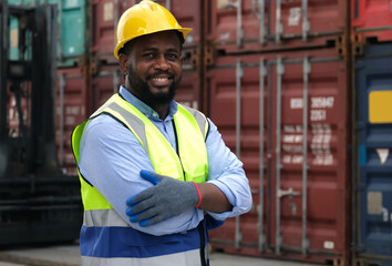Black worker wearing hard hat looking at camera and cross his arms  with background of cargo...
