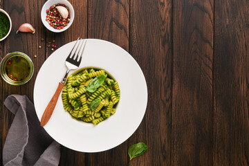 Italian Fusilli Pasta with Pesto. Fusilli pasta with basil pesto and herbs, parmesan cheese, basil and garlic on white plate on old wooden table background. Top view. Copy space. Mock up.