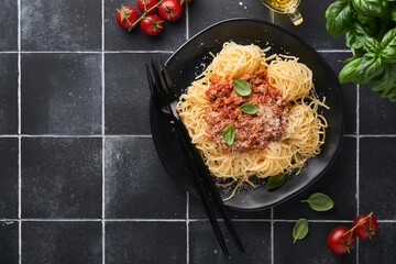 Tagliatelle pasta with meatballs in tomato sauce, basil and parmesan cheese on black stone or concrete background. Traditional Italian dish and cuisine. Top view with copy space.