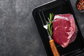 Beef steak. Fresh raw beef steak with fork and rosemary in vacuum black plastic pack on black stone...