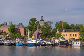 Fototapeta premium Small ships and boats at a pier on the island Skeppsholmen, a church tower and old military buildings sunny summer morning in Stockholm
