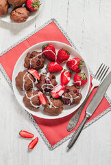 Freshly baked chocolate muffins with cream, cranberries and strawberries on a white plate. Plate with muffins on a red napkin on a white background. Top view.