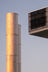 Closeup of two metallic smoke stacks and a air conditioning exhaust grille during the sunset