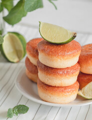 Stacked fresh donuts with green lime and mint on a table. Breakfast with golden doughnuts.