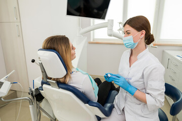 A beautiful female dentist is talking to a patient while sitting in a chair.