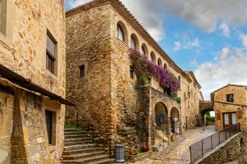 A small shop with purple bougainvillea bushes in the medieval walled village of Pals Spain, on the Costa Brava coast. - obrazy, fototapety, plakaty