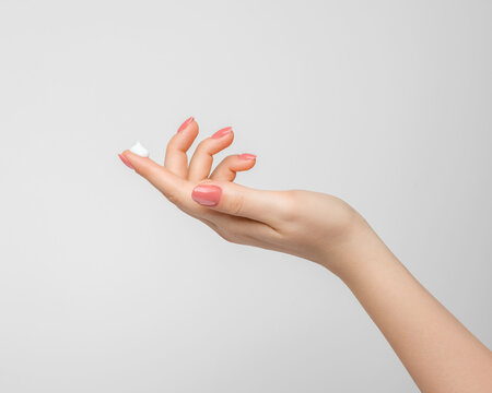 A drop of thick white hand cream on the finger of a woman's hand. Groomed hands, natural short nails with nude nail polish, on a light background.