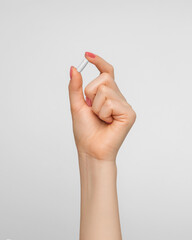 Pill in a capsule in a woman's hand with nude nail polish.