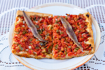 Tomato and vegetable pizza with anchovies, on a white plate, on a crochet tablecloth