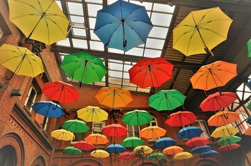 Fototapeta na wymiar Bunte Regenschirme unter Glasdach von hohem großen Gebäude 