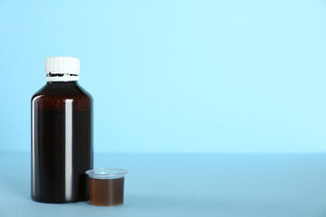 Bottle of cough syrup and measuring cup on light blue background. Space for text