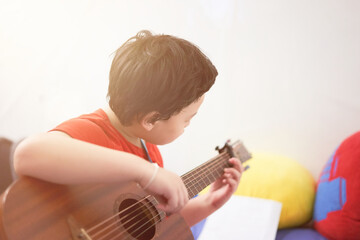 The boy plays the guitar with his left hand, a song by himself, on the sofa, in the bedroom,...