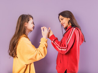 Happy smiling beautiful playful mother and cute daughter have the peace and love in fashion trendy hoodie together on purple studio background with empty copy space. Happy