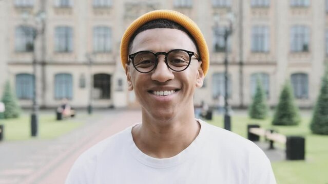 A portrait of an African American student in glasses smiling at the camera with the university on the background