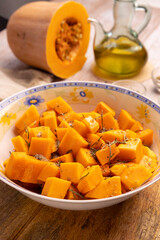 Diced pumpkin pieces in a bowl, with spices and olive oil
