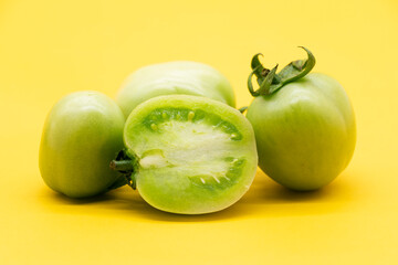Whole and halved green unripe tomato isolated on yellow background