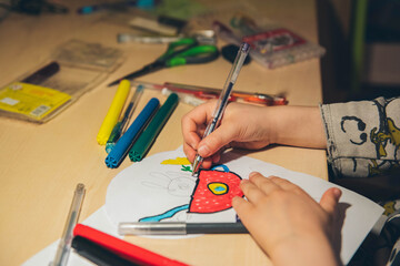 A little girl draws at home in the evening. Children creativity.