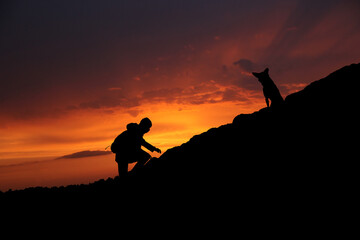 Sylwetki człowieka i psa na skale, zachód słońca w tle