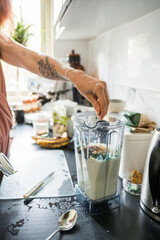 Woman standing near the table and preparing smoothie for the breakfast