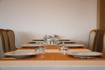 A restaurant consisting of brown wooden chairs and a table with a white fabric cover. Empty catering plates and forks, spoons, knives on a white tablecloth.	
