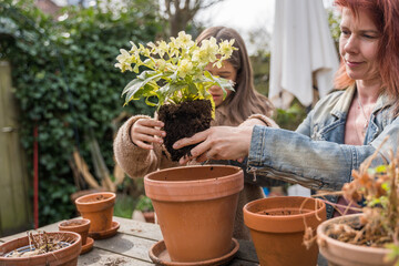 Girl preparing soil for plants and replacing flowers while spending time with her mom