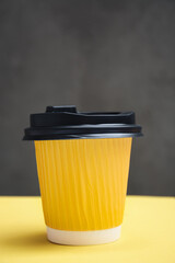 Yellow paper cup with takeaway coffee. Container on a yellow and dark gray background. Concept of adding taste and color to life. Copy Space for text