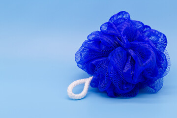 Blue mesh pouf bath sponge washcloth single object on blue background closeup photo with copy space. Soft synthetic shower wash cloth. Washing hygiene design element. Spa body care accessory product.