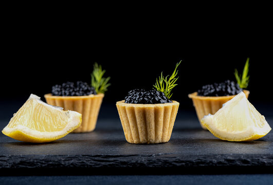 Tartlets with black caviar and slices of lemon on a stone board for serving.