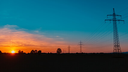 Beautiful sunset with a dramatic sky and overland high voltage lines near Tabertshausen, Bavaria, Germany