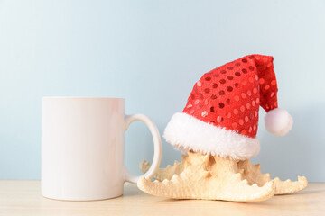 Obraz na płótnie Canvas White coffee mug mockup of Christmas in July. Cup and starfish in Santa hat