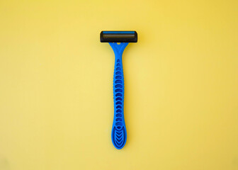 A blue disposable razor lies on a yellow background