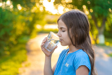 The child drinks water from a glass. Selective focus.