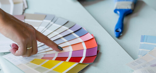 The hands of a female designer choosing paint samples for walls. A girl looks at a color sample to...