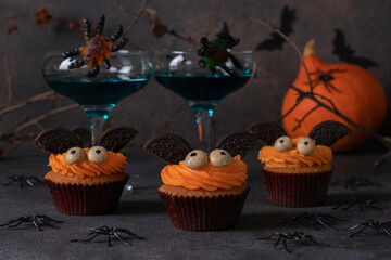 Halloween treat - bright sweet cakes in the shape of bats on dark brown background with decor