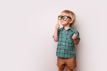 a little cute blond boy in big glasses and a green checkered shirt stands against a white wall, preschool education, kindergarten, school for talented children, nerd, elementary school, place for text