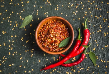 Wall murals Hot chili peppers Dry chili pepper flakes and fresh chili peppers. Bowl of crushed hot red pepper, dried chili flakes top view on wooden dark background.