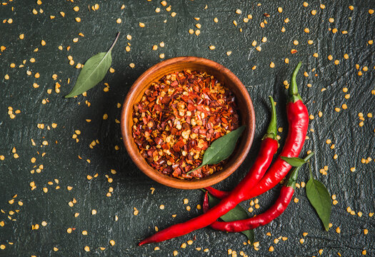 Dry chili pepper flakes and fresh chili peppers. Bowl of crushed hot red pepper, dried chili flakes top view on wooden dark background.