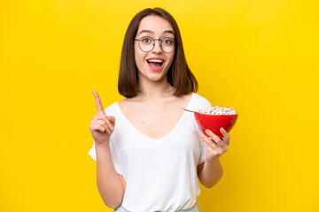 Young Ukrainian holding a bowl of cereals isolated yellow background pointing up a great idea