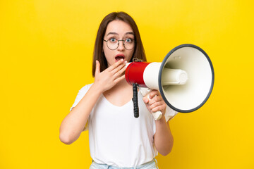 Young Ukrainian woman isolated on yellow background shouting through a megaphone with surprised expression