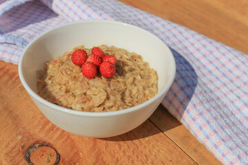 Oatmeal with wild berries close-up on a wooden table. In the background is a checkered kitchen towel.