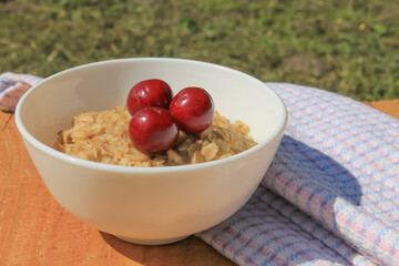 Oatmeal with cherries in a white plate unfolds. Red berries are good for health. Kitchen towel in the background.