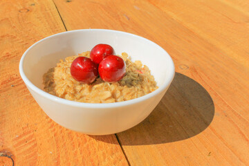 Oatmeal with cherries in a white plate on a wooden table, isolated. In a healthy body healthy mind.