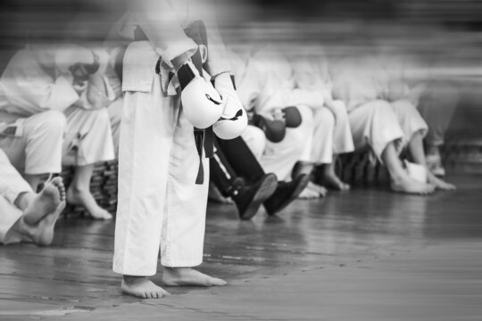 Sportsman karateka in a white kimano is preparing for a duel. Vintage style with film noise and motion blur. Focus on gloves in hands.