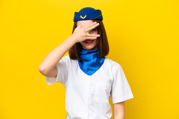 Airplane stewardess Ukrainian woman isolated on yellow background covering eyes by hands and smiling