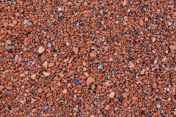 Ground texture with small multi-colored stones. Pebbles of red and terracotta color. Stone decoration of sidewalks and footpaths in parks, squares and courtyards. Perfect for background and design.