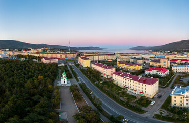 Aerial view of a northern seaside town. Top view of the streets, buildings and the chapel. In the distance the sea bay and mountains. Beautiful morning cityscape. Magadan city, Magadan Region, Russia.