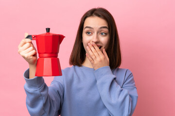 Young Ukrainian woman holding coffee pot isolated on pink background with surprise and shocked...